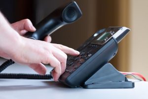 Hand dialing office phone representing call to action and customer contact services
